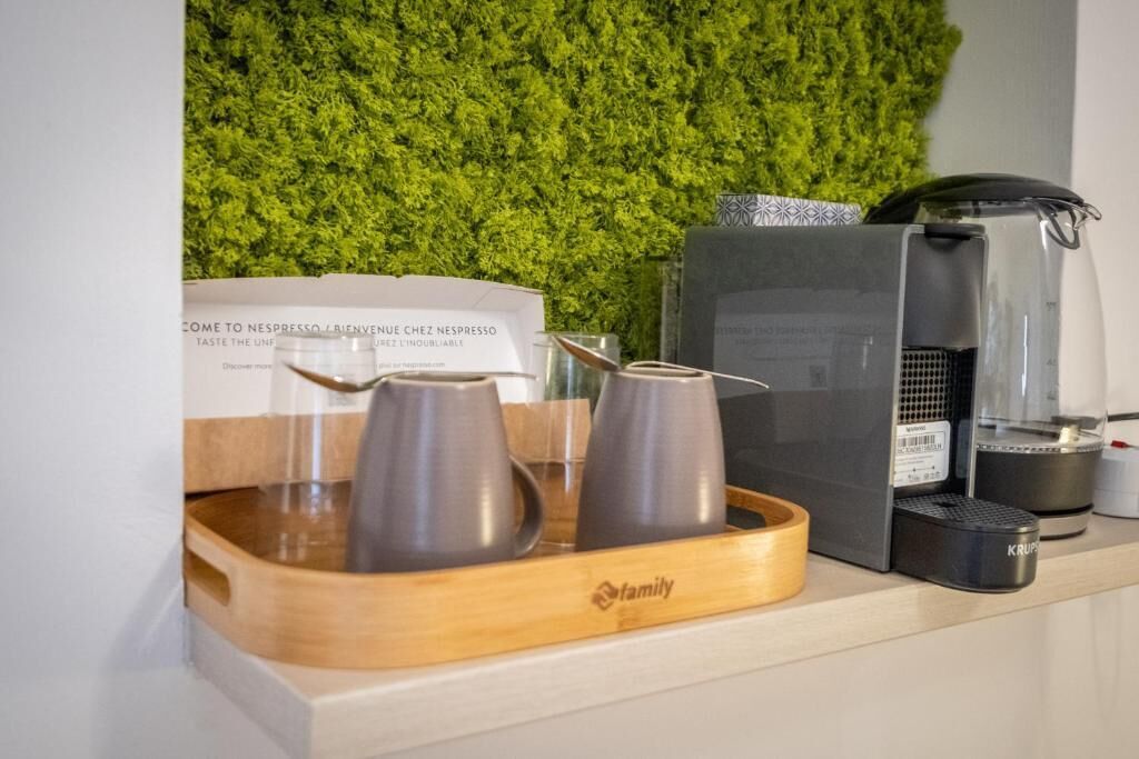 Ein Kaffee-Bereich mit Kaffeemaschine, einer Krups-Kaffeemühle und einem Schild, das Gäste in die Nespresso Lounge einlädt.