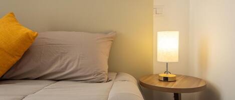 Una cama con una almohada, una mesita de noche con una lámpara y un interruptor de pared.