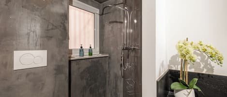 A bathroom with a shower, a toilet, a sink with a potted orchid, and a towel rack.