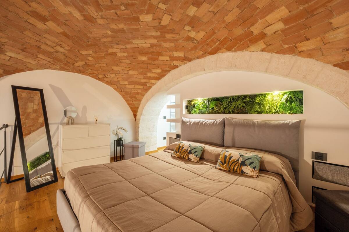 Ein Schlafzimmer mit Ziegeldecke, einem Bett mit beige farbenem Quilt und einer an der Wand befestigten Zimmerpflanze.
