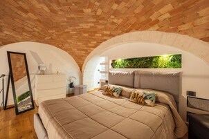 Un dormitorio con techo de ladrillo, una cama con colcha color beige y una planta verde montada en la pared.