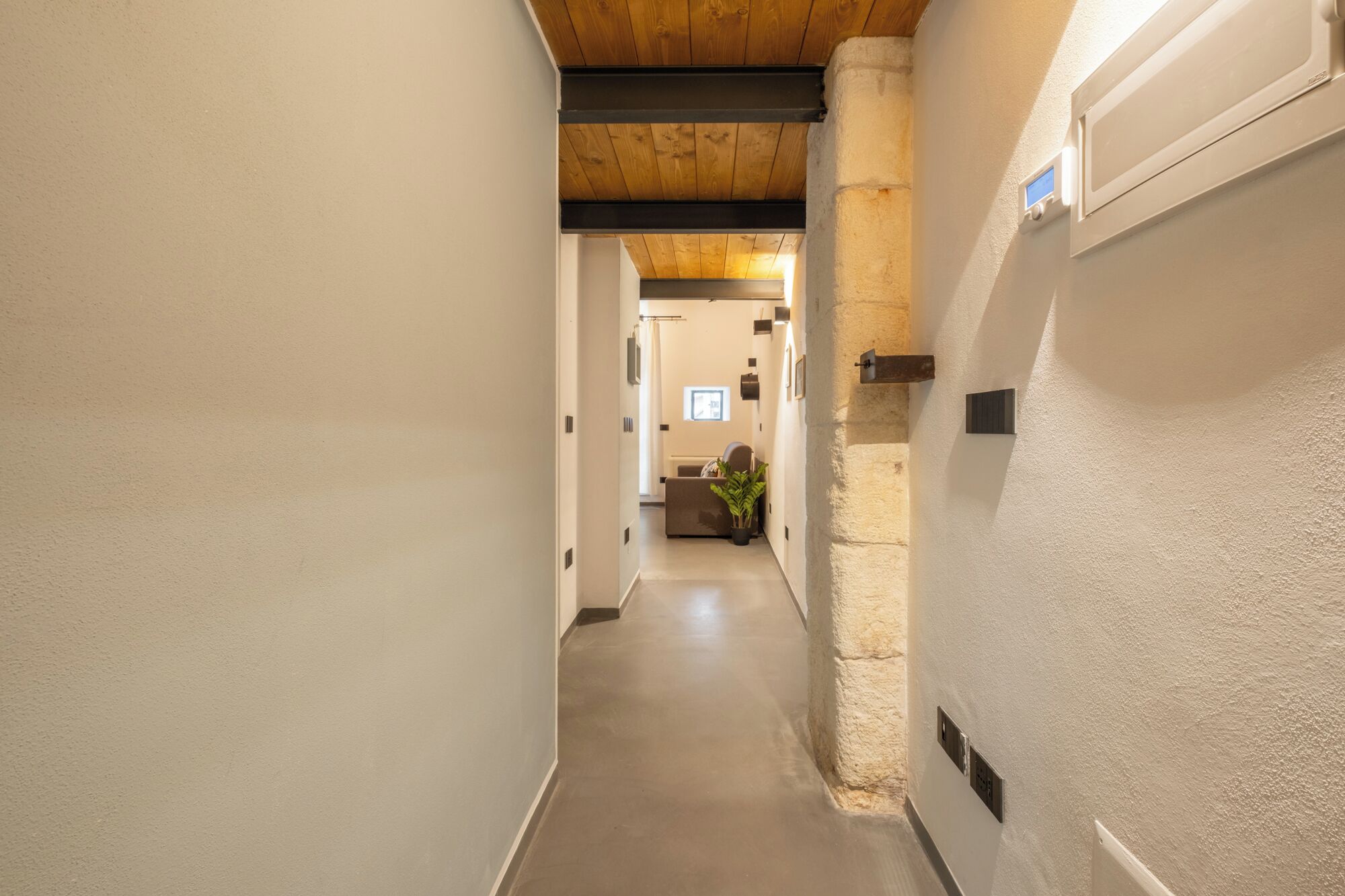 A narrow hallway with a wooden ceiling, white walls, and a door on the right.