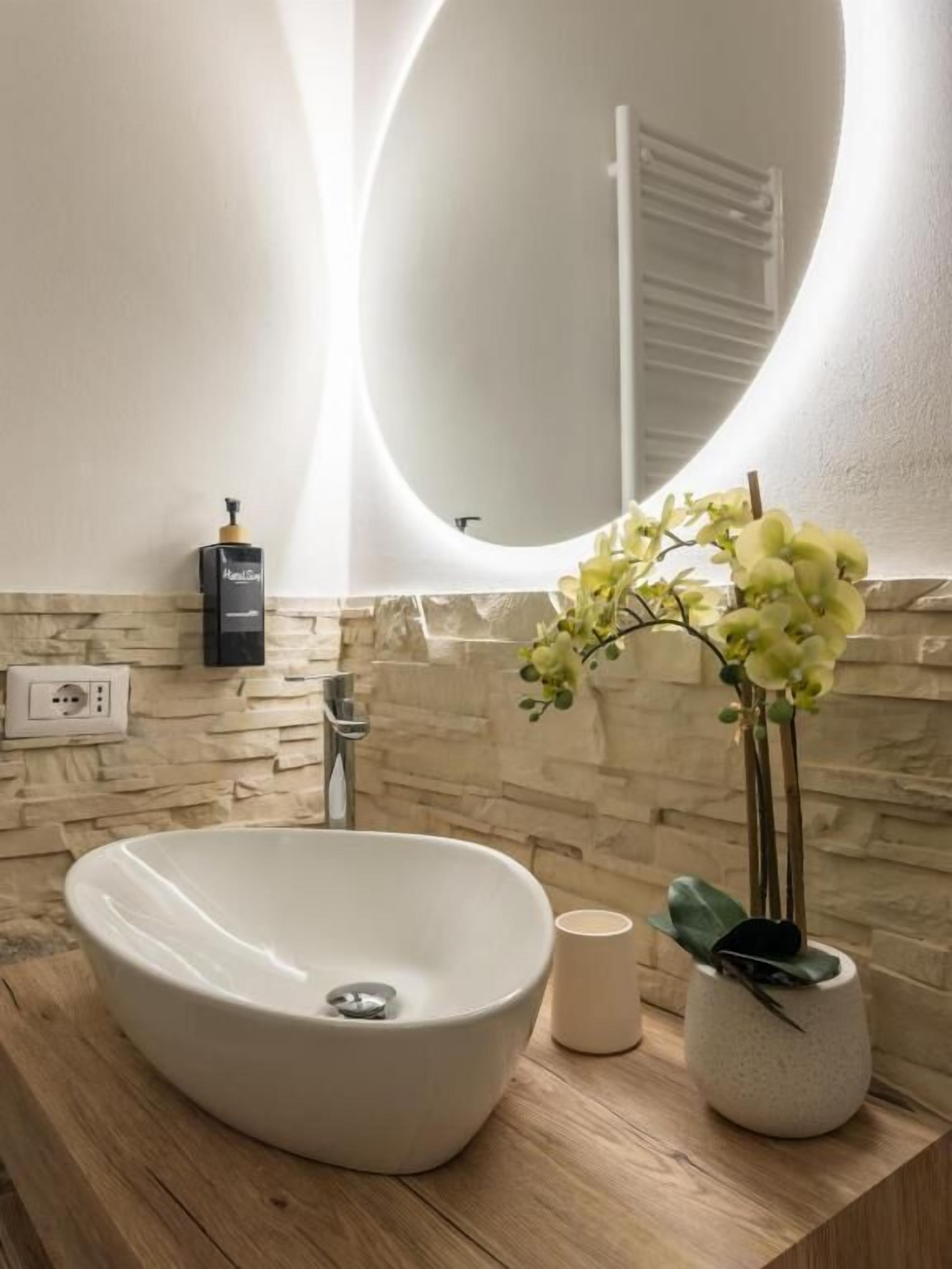 A bathroom with a white sink, a round mirror, a wall-mounted heater, and a potted plant.