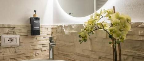 Un baño con un lavamanos blanco, un espejo redondo, un calentador de pared y una planta en maceta.