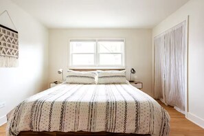 A bedroom with a bed, two bedside tables, a window, and a curtain.