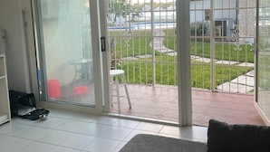 Una habitación con puerta de vidrio corredera que da a un patio con suelo de baldosas y una pequeña mesa.