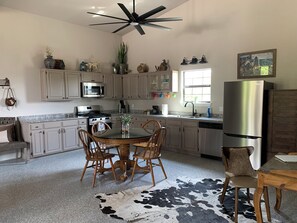 A kitchen with a dining table, chairs, a ceiling fan, cabinets, a refrigerator, and a window. - Brooks Barndo (Boerne)
