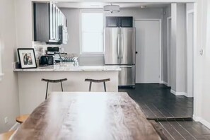 A modern kitchen with stainless steel appliances, a marble countertop, and a dining area with a wooden table and two chairs.