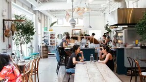 Un moderno caffè con un lungo bancone in legno, posti a sedere per diverse persone e una zona cucina sullo sfondo.