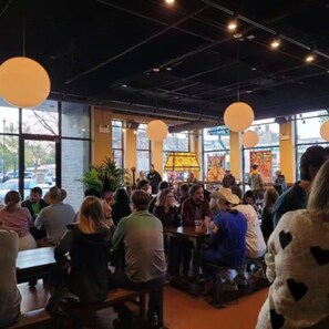 A restaurant interior with round tables, large windows, and hanging lights.