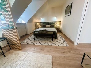 A bedroom with a sloped ceiling, a bed with a geometric-patterned rug, a bedside table, and a wall-mounted lamp. - Les Trois Mouettes – Spacious Family Apartment (Saint-Brieuc)