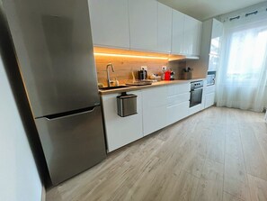 A modern kitchen with stainless steel appliances, white cabinetry, and a wooden floor. - Les Trois Mouettes – Spacious Family Apartment (Saint-Brieuc)