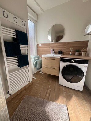 A compact kitchen with a built-in washing machine, a small sink, and a mirror above it. - Les Trois Mouettes – Spacious Family Apartment (Saint-Brieuc)