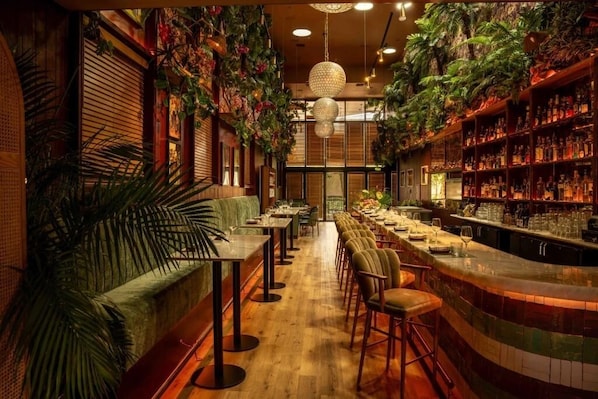 A bar area with wooden flooring, bar stools, and shelves stocked with bottles.