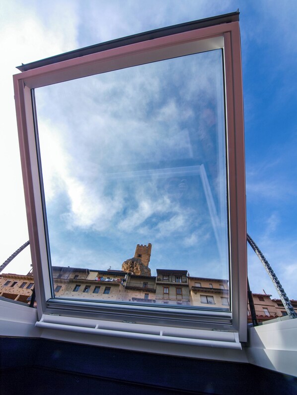 Una ventana con vistas despejadas a una torre de piedra histórica y edificios al fondo.