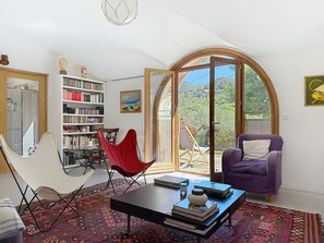 A spacious living room with a large bookshelf, a red chair, a purple armchair, and a view through a glass door to the outdoors. - Very nice apartment in a pretty village house (Pigna)
