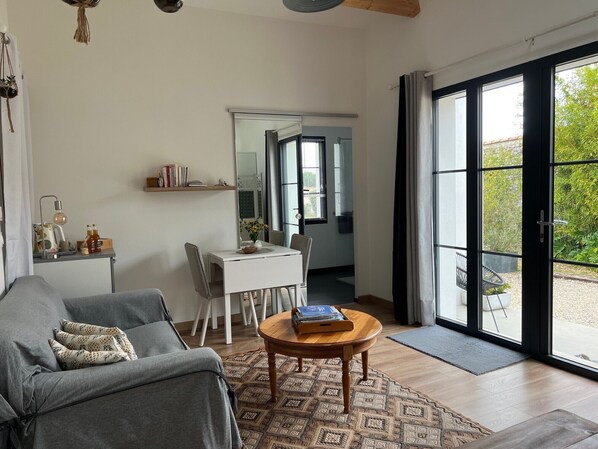 A modern living room with a sofa, a dining table, a coffee table, and a large sliding glass door leading to an outdoor area.