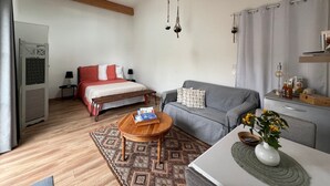 A modern living room with a bed, sofa, wooden coffee table, and a dining area with a table and chairs. - Guest Room “Chambre De Lucie” with Private Terrace, Garden, and Wi-Fi (Bourcefranc-le-Chapus)