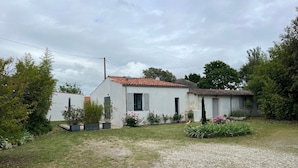 A white building with a red-tiled roof, surrounded by a gravel driveway and a grassy area with flowering plants. - Guest Room “Chambre De Lucie” with Private Terrace, Garden, and Wi-Fi (Bourcefranc-le-Chapus)