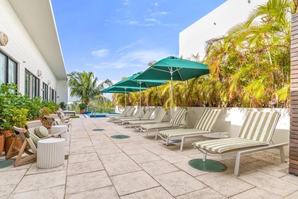 A poolside area with lounge chairs and umbrellas, surrounded by palm trees and potted plants.