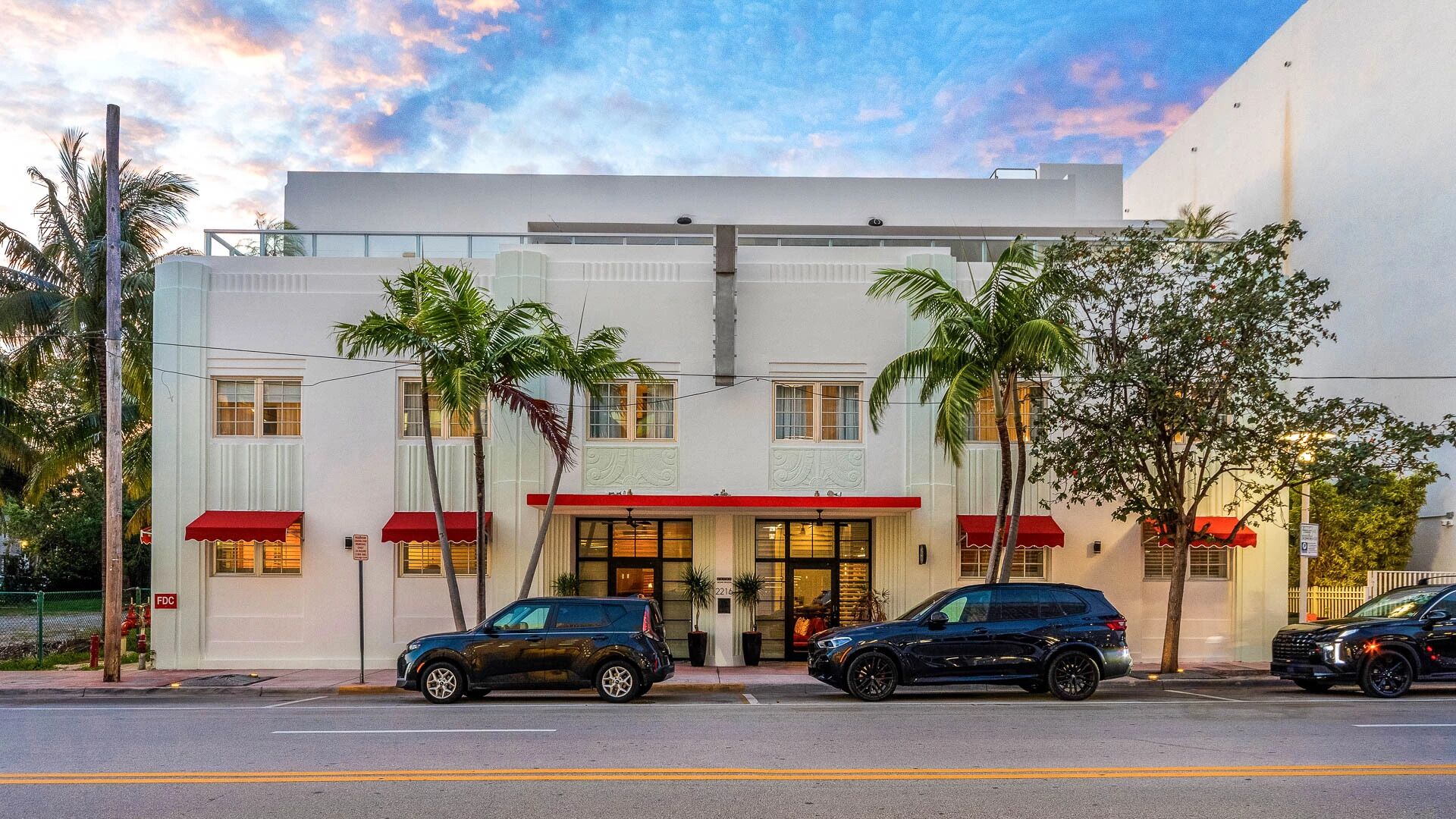 A two-story building with a flat facade, red awnings, and palm trees in front.