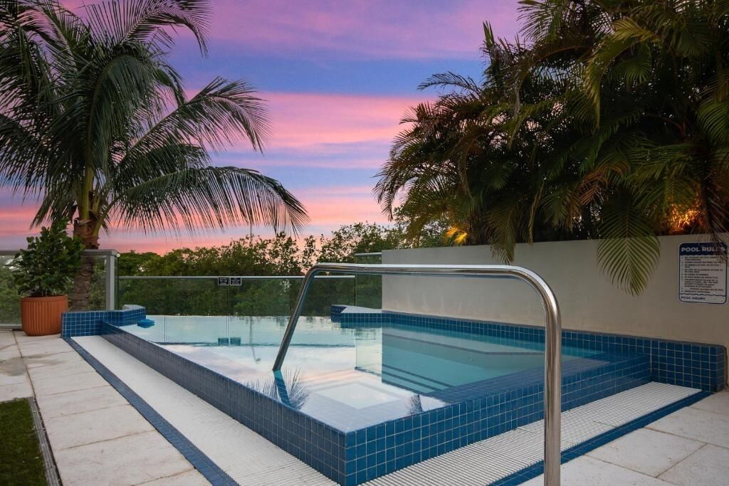 Ein Pool mit Glasbarriere, umgeben von Palmen und einem Sonnenuntergangshimmel.
