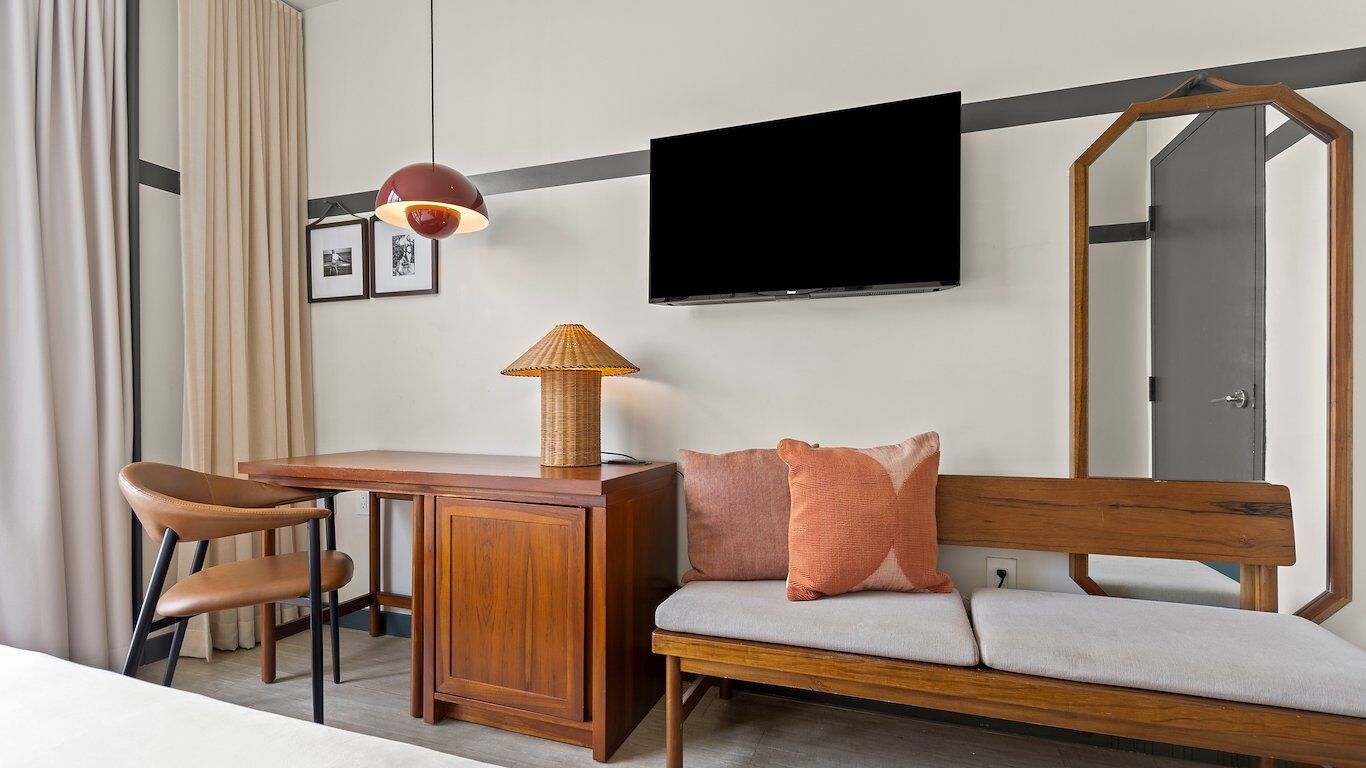 A hotel room with a wooden desk, a chair, a sofa, a television, and a lamp.
