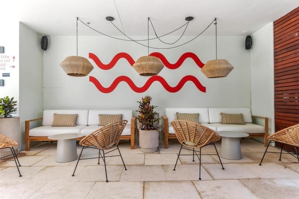 Zona d'estar moderna amb un sofà blanc, cadires de vimet i un dibuix on un patró d'ones vermelles decora la paret.