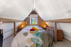 A bedroom with a sloped ceiling, a window, a bed with a patterned bedspread, bedside lamps, and a wicker chest of drawers. - Cottage 'Le Saulou' with Private Terrace and Private Garden (Sarlat-la-Canéda)