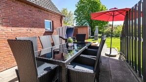 An outdoor patio with wicker furniture, a glass-top table, and a red umbrella.