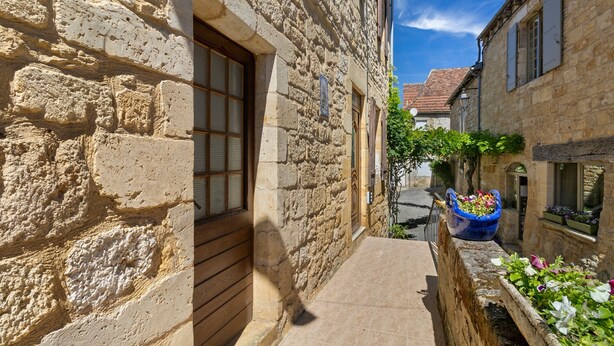 Ein schmaler Steinweg zwischen Gebäuden mit einem Fenster und einem Blumenkasten.