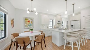 Una cocina moderna con armarios blancos, una isla central y un comedor con sillas.