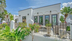 Un edificio moderno con amplios ventanales, un patio amurallado con mobiliario exterior y plantas tropicales.