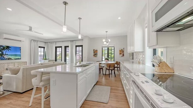 Una cocina moderna con una isla central, armarios blancos y un comedor con mesa y sillas.