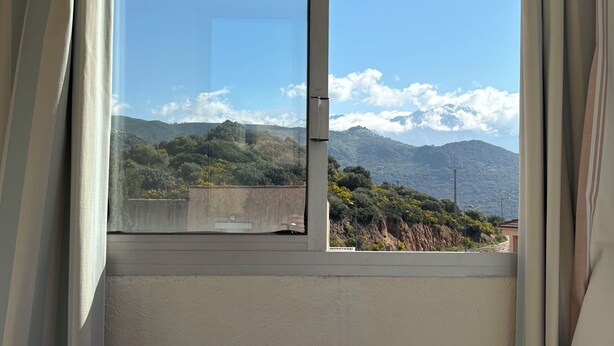 A room with a large window, a chair, and a table with a colorful tablecloth. - PROMO - Sea & mountain view - 6p - parking - Linen included (Corbara)