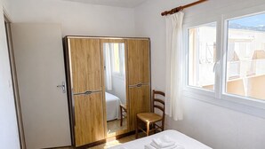 A hotel room with a bed, a wooden wardrobe, a small table with a chair, and a window with curtains. - PROMO - Sea & mountain view - 6p - parking - Linen included (Corbara)