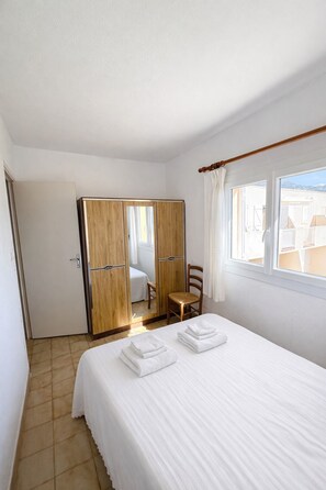 Ein Hotelzimmer mit Bett, einem Holzschrank, einem kleinen Tisch mit Stuhl und einem Fenster mit Vorhängen.