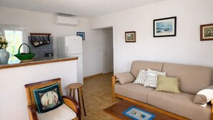 A living room with a sofa, a chair, a coffee table, a kitchen area with a refrigerator, and a door leading to another room. - PROMO - Sea & mountain view - 6p - parking - Linen included (Corbara)