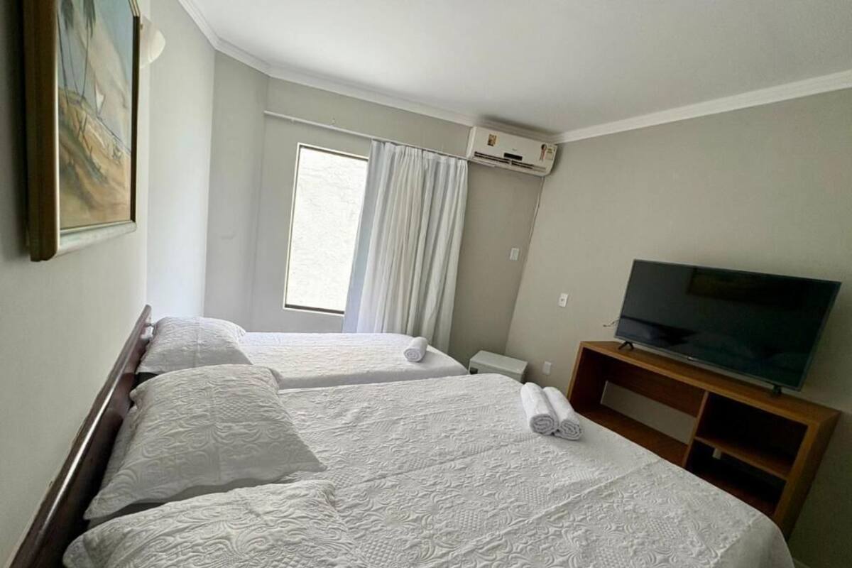 A hotel room with two beds, a television, and an air conditioning unit.