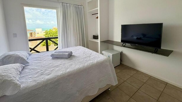 A bedroom with a bed, a TV, a window with curtains, and a balcony. - BREEZE HOTEL (Natal)