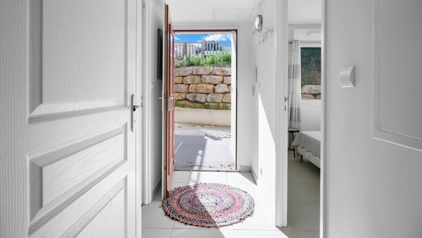 Een gang met een deur die leidt naar een kamer met een bed en een stenen muur.