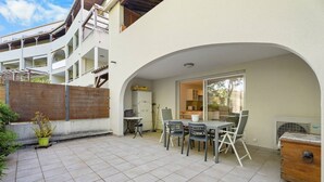 Een terras met een tafel en stoelen, een houten kist, en uitzicht op een gebouw met balkons.