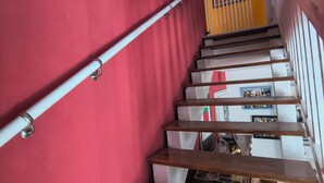 Eine Treppe mit Metallgeländer, Holzhinweisen und einer roten Wand mit farbenfrohen Kunstwerken.