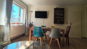 Ein Essbereich mit einem Glastisch, Stühlen, einem an der Wand montierten Fernseher und einer Vitrine.