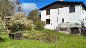 Ein zweigeschossiges Haus mit weißer Fassade und braunem Dach, umgeben von einem Garten mit verschiedenen Pflanzen und Blumen.
