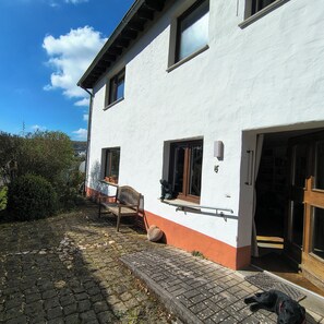 A two-story house with a white exterior, a wooden bench, and a black dog lying on the ground.