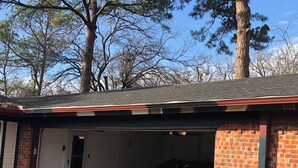 A garage with a car parked inside, a brick exterior, and trees in the background. - Serene 3-bedroom house with AC, on-site laundry in welcoming Arlington (Arlington)