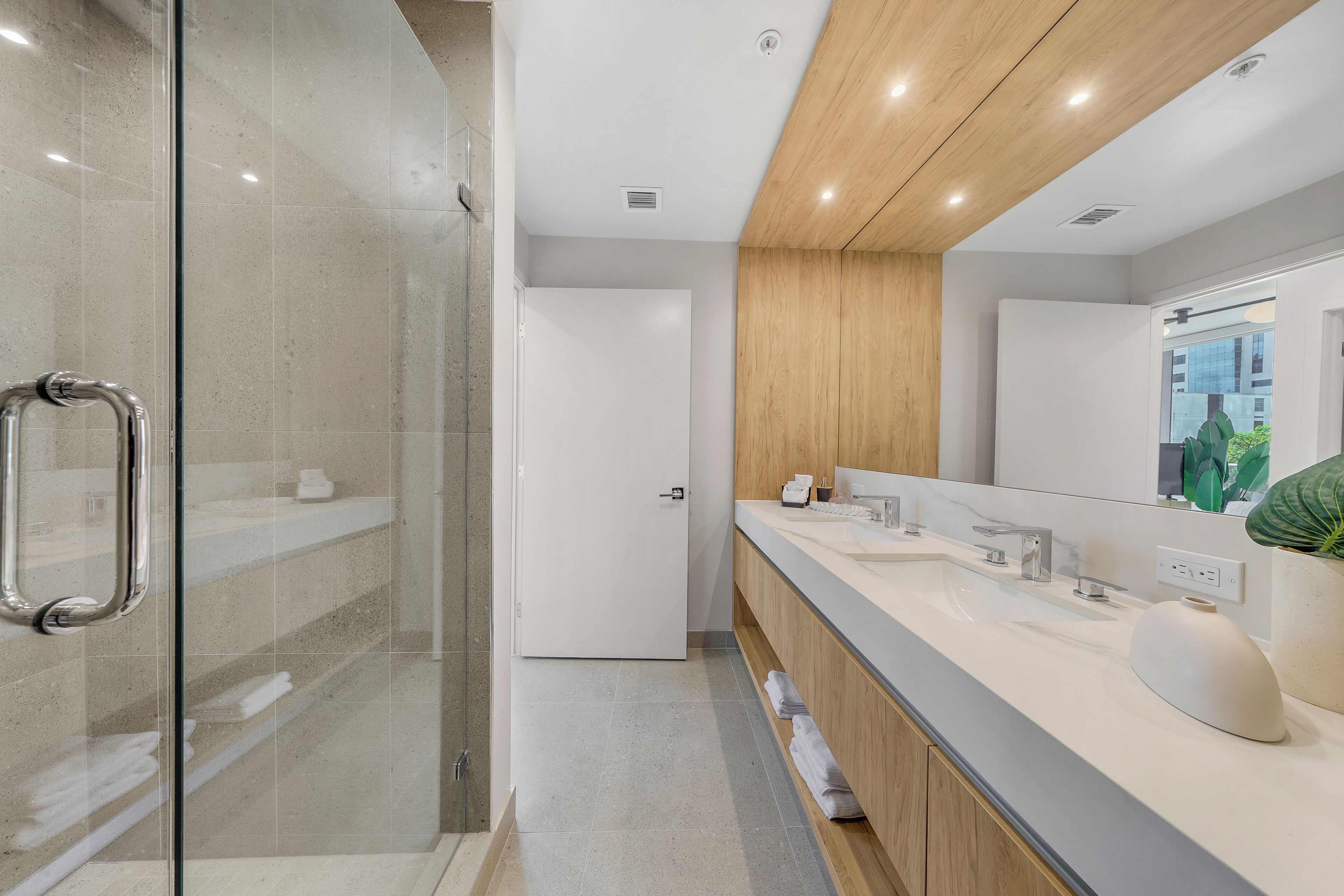 A modern bathroom with a glass shower enclosure, a wooden vanity, and a large mirror.