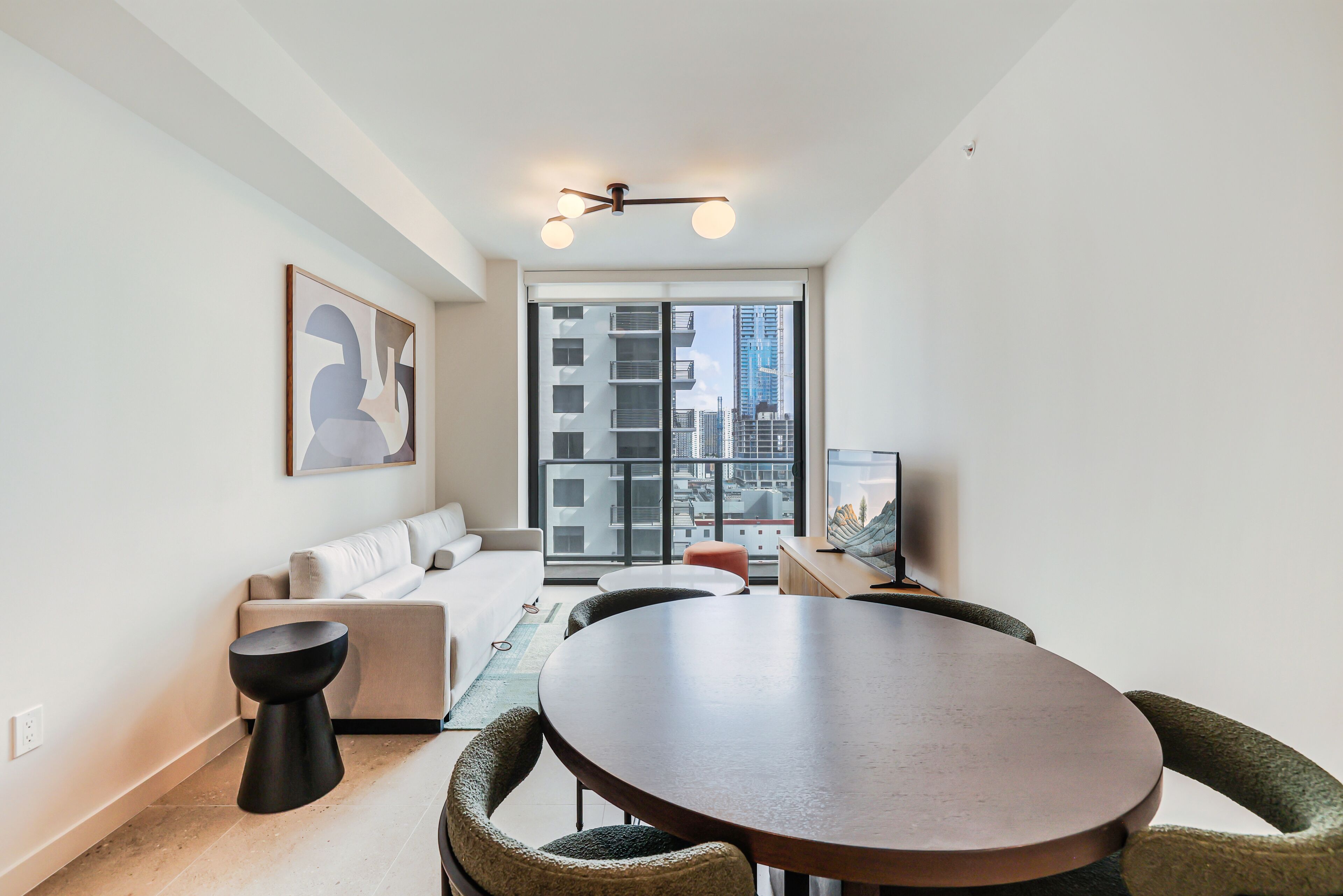 A modern living room with a round table, a sofa, and a large window with a city view.