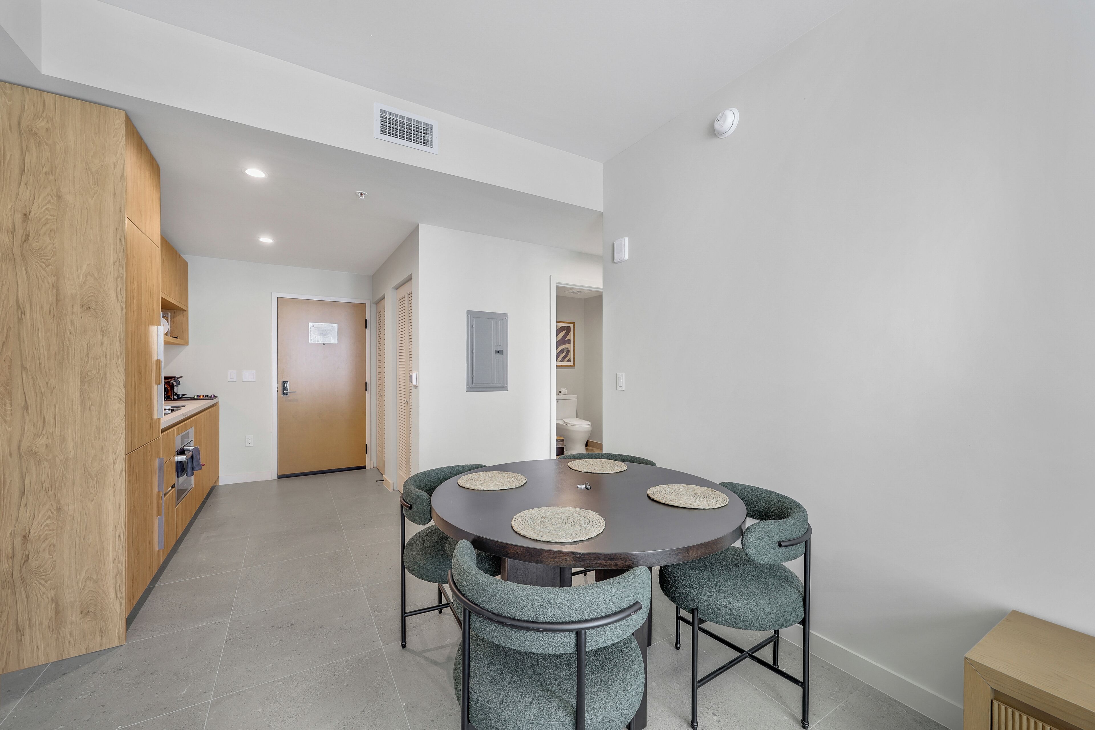 A modern dining area with a round table, six chairs, and a kitchen with wooden cabinets.